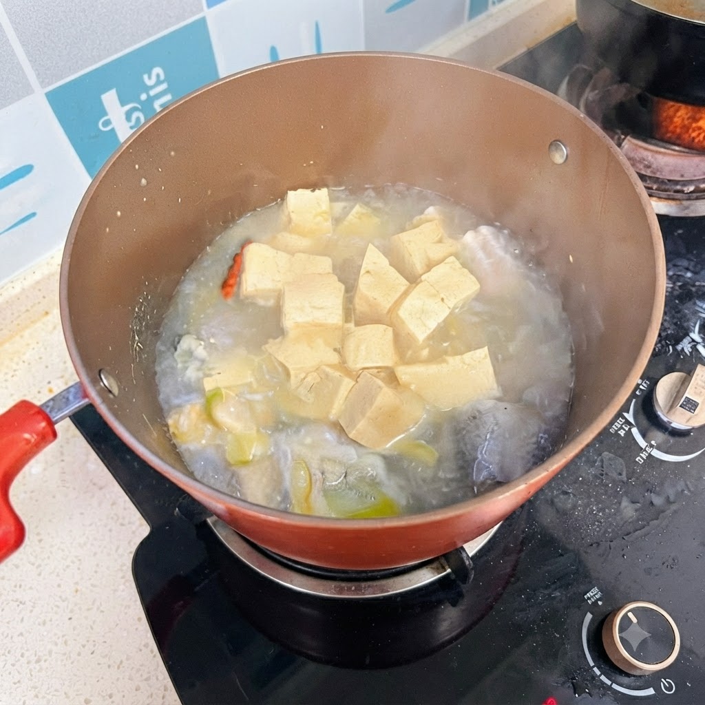 Ein Topf mit Fisch- und Tofusuppe köchelt auf dem Herd mit einer milchig-weißen Brühe.