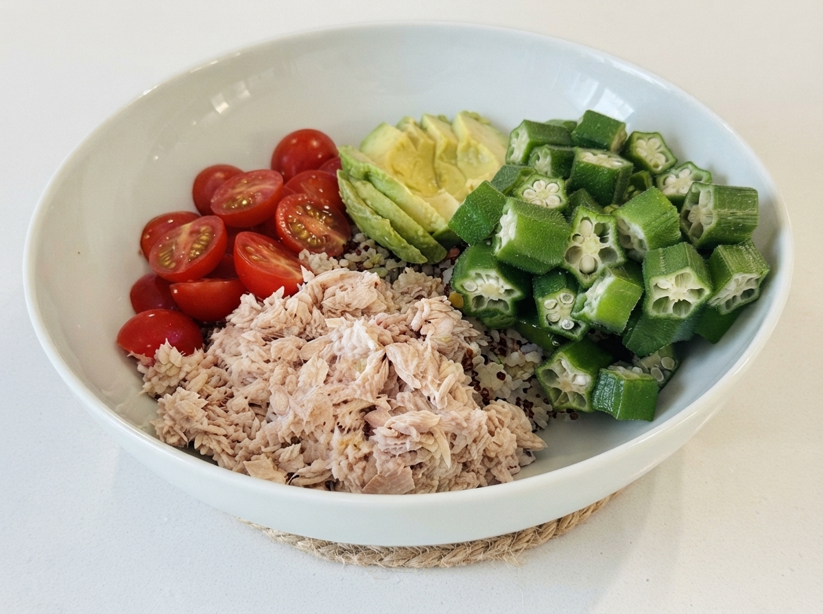 Eine weiße Schüssel mit Reis als Basis, darauf fein säuberlich angerichteter Thunfisch, Kirschtomaten, in Scheiben geschnittene Avocado und Okra.