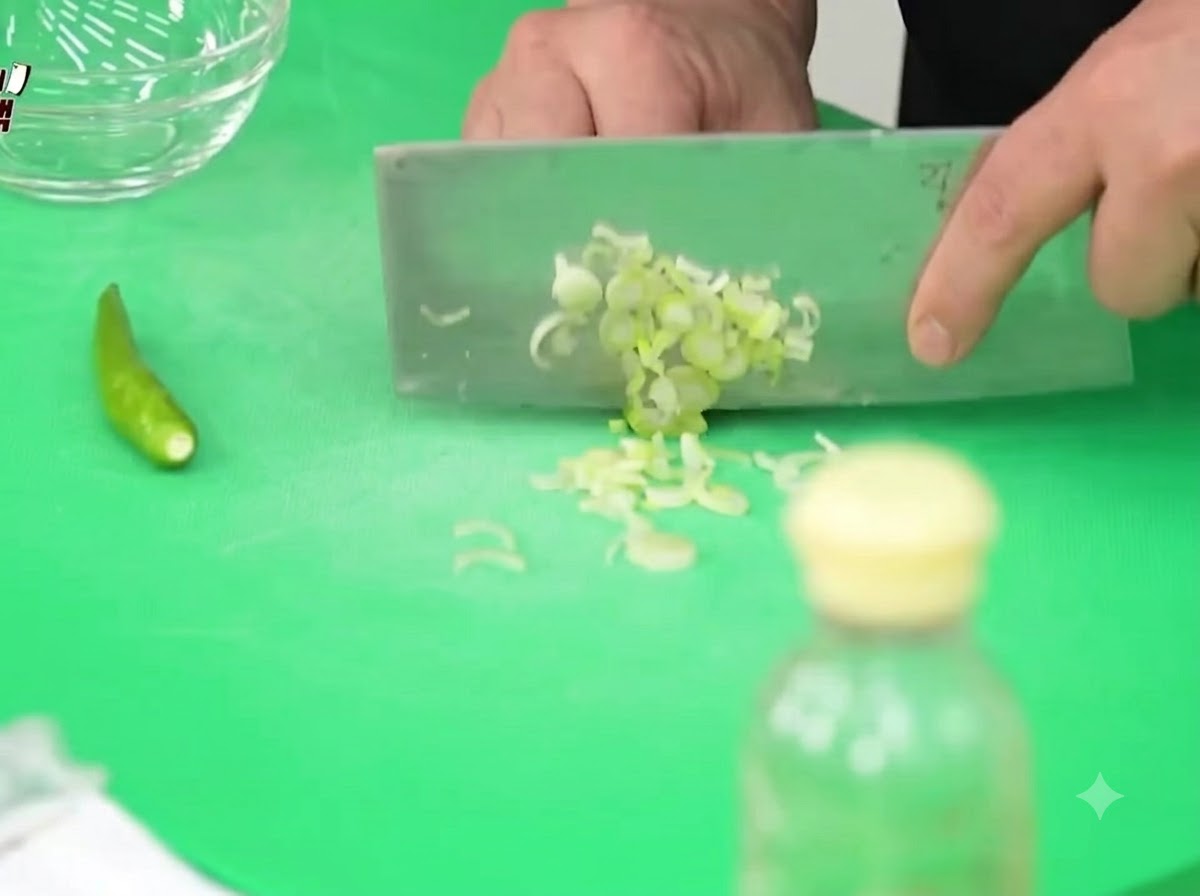 Frühlingszwiebeln, Cheongyang-Chilis und Zwiebeln werden auf einem grünen Schneidebrett mit einem Hackbeil fein gehackt.