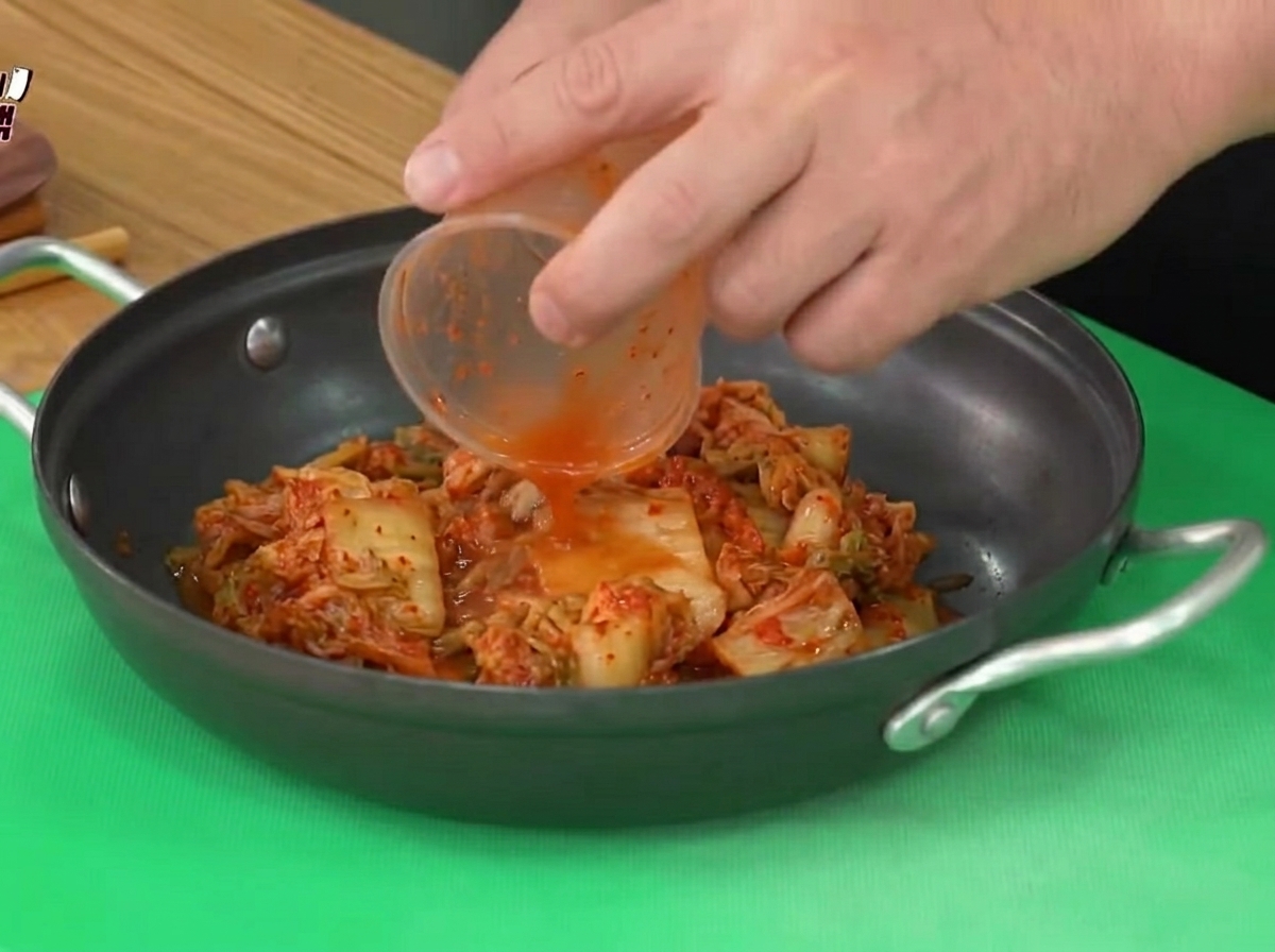 Saures Kimchi wird aus einem Plastikbehälter in einen schwarzen Kochtopf gegeben.