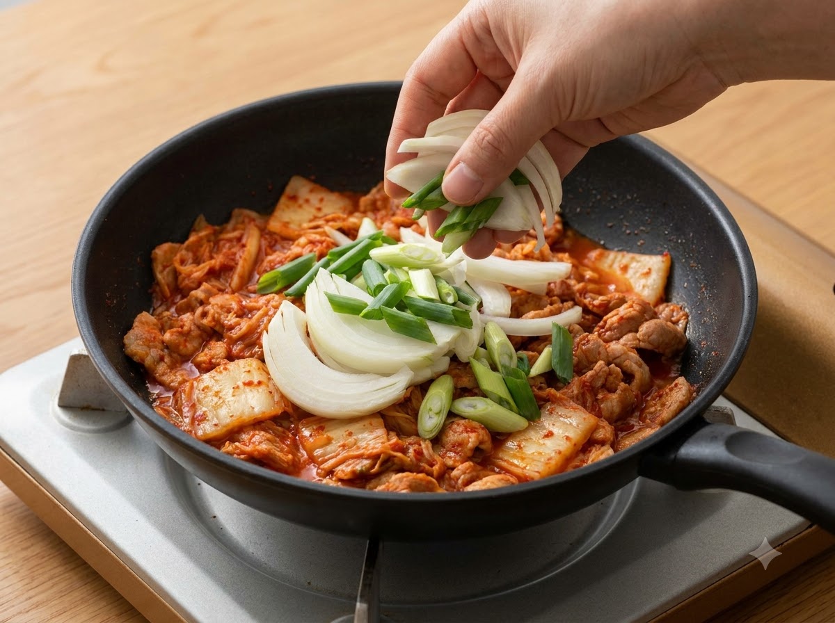 Geschnittene Zwiebeln und Frühlingszwiebeln werden über das Kimchi in den Topf gegeben.