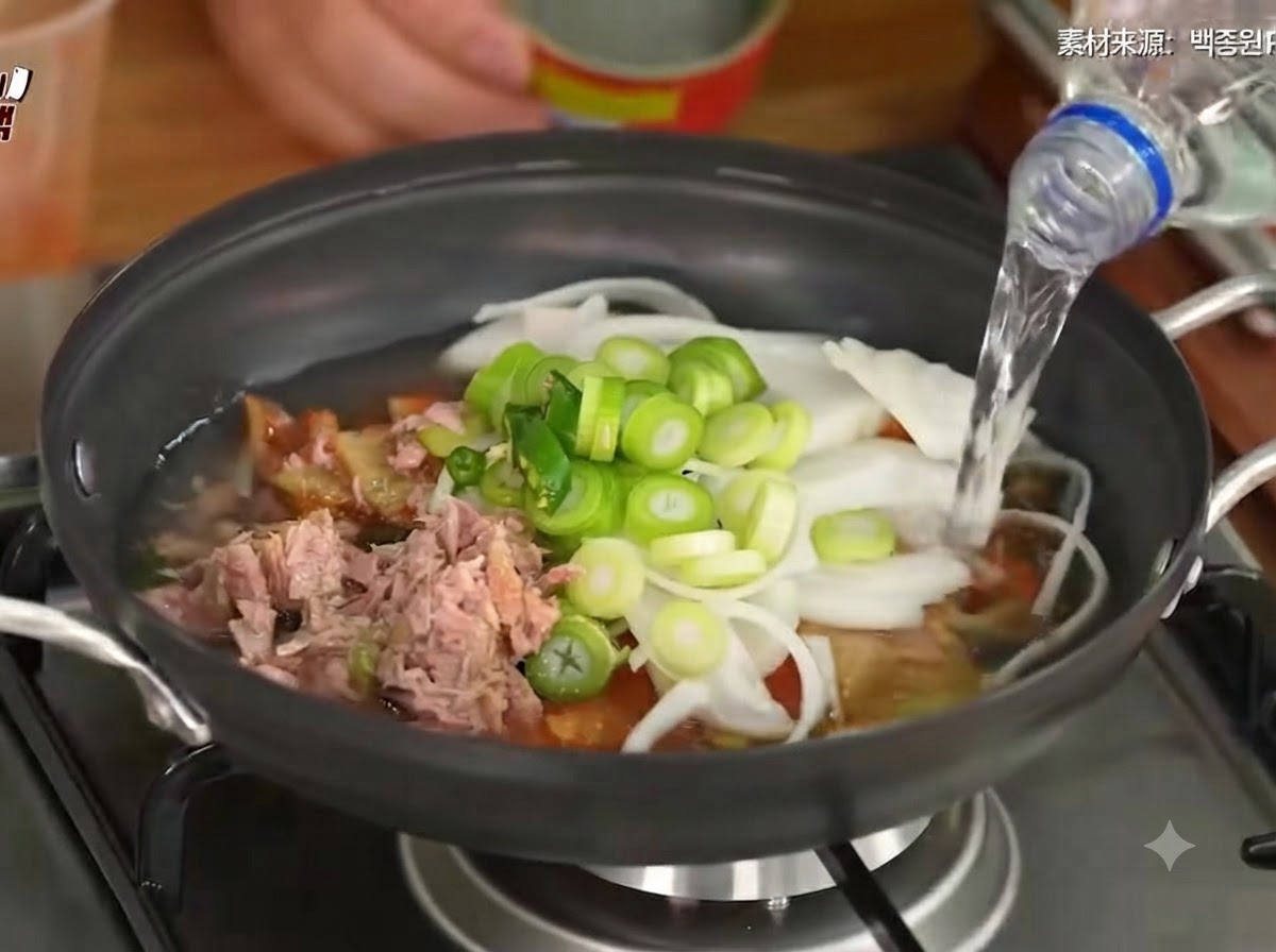 Wasser wird in den Topf gegossen, der Kimchi, Gemüse und Thunfisch enthält.