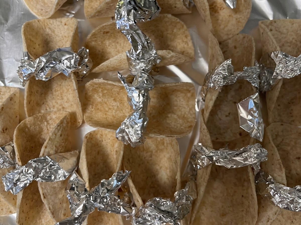 Kleine Tortilla-Wrappers, gestützt und gesichert mit Alufolienstücken auf einem Backblech bereit für den Ofen.
