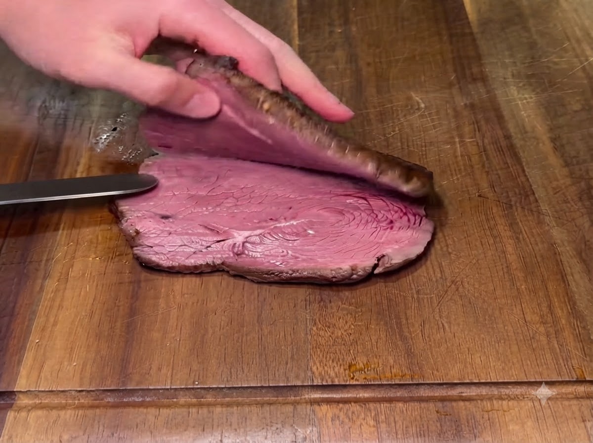 Ein gebratenes Steak wird mit einem Messer waagerecht auf einem Holzschneidebrett halbiert.