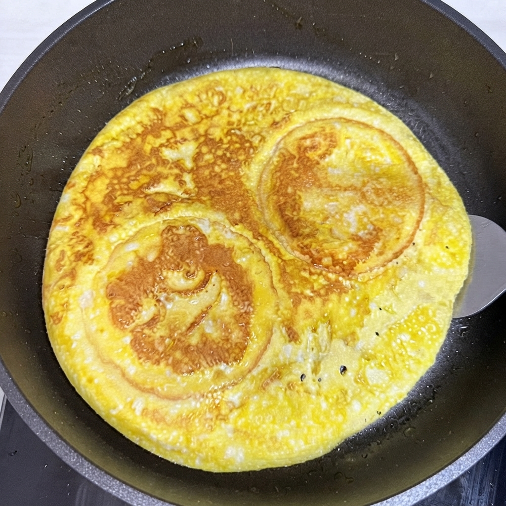 Ein Pfannenwender wendet eine runde, gebratene Ei- und Burgerbrötchen-Schicht in einer Bratpfanne.