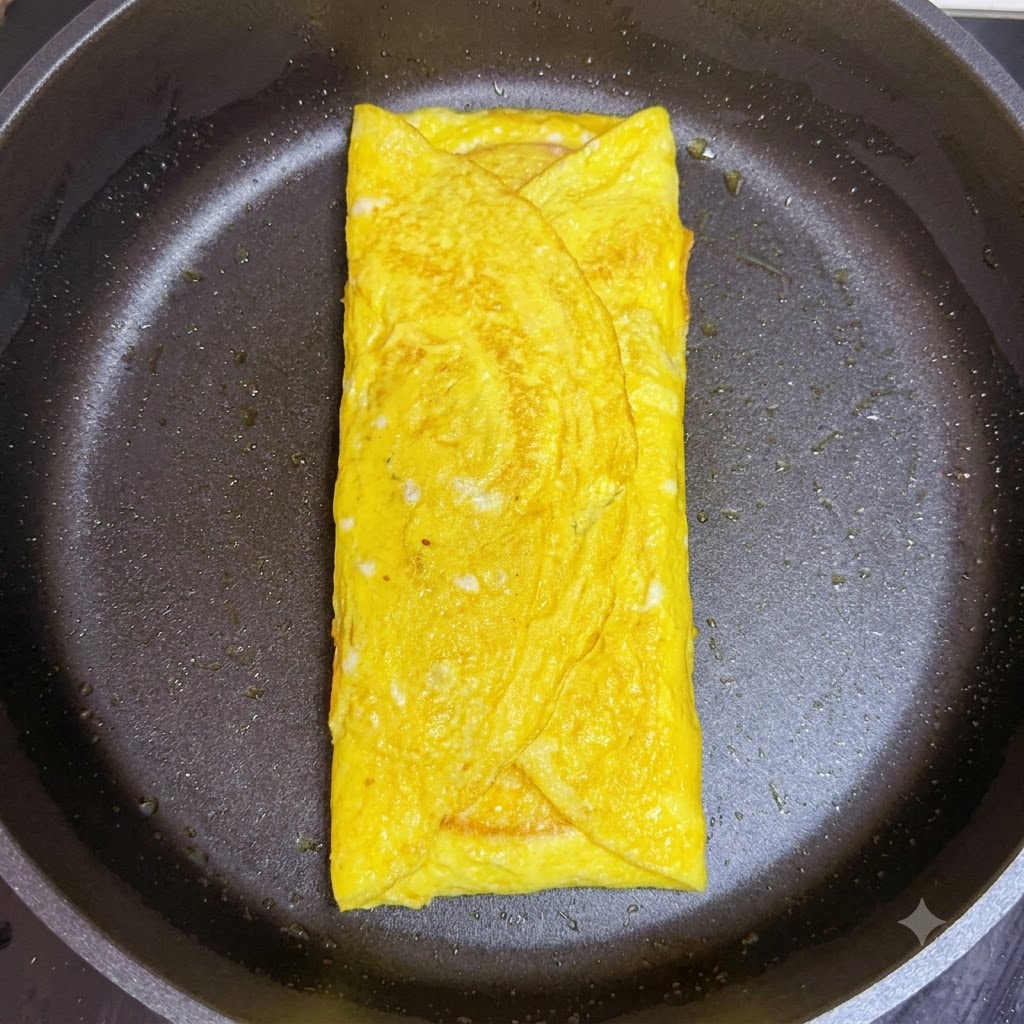 Eine gefaltete Scheibe rosa Schinken wird in der Pfanne auf den Käse im Eier-Wrap gelegt.