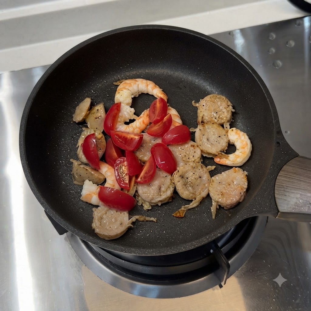 Kirschtomaten und geschnittene grüne Paprika vermischt mit Wurst und Garnelen in einer Bratpfanne.