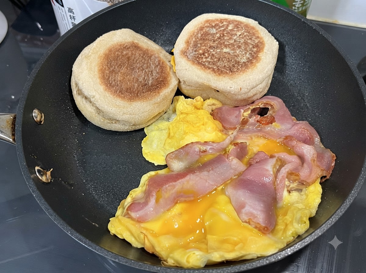 Eier stocken in einer Pfanne mit Baconscheiben und daneben liegenden English Muffins.
