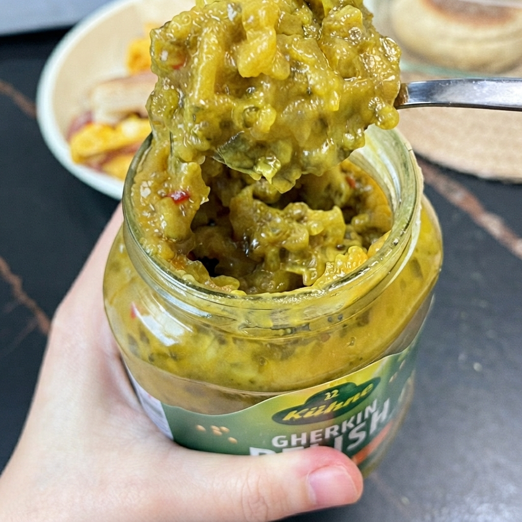 Ein Löffel hellgrünes Gewürzgurken-Relish wird mit einem kleinen Löffel aus einem Glas gehoben.