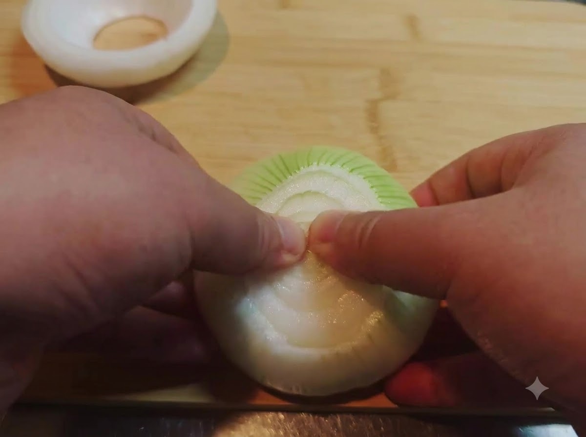 Hände drücken und entfernen die inneren Schichten einer Zwiebelhälfte, um einen hohlen Zwiebelring zu formen.