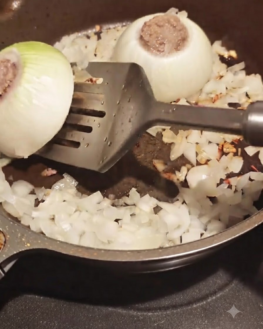 Ein Pfannenwender wendet einen fleischgefüllten Zwiebelring in einer Bratpfanne mit umgebenden gehackten Zwiebeln.