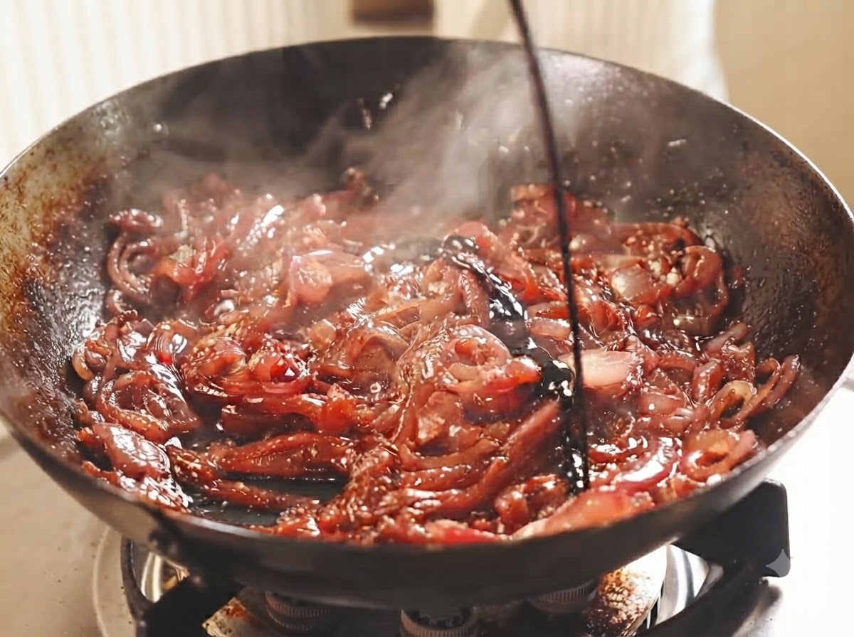 Geschnittene rote Zwiebeln schmoren in einem Wok mit Wein und Essig.
