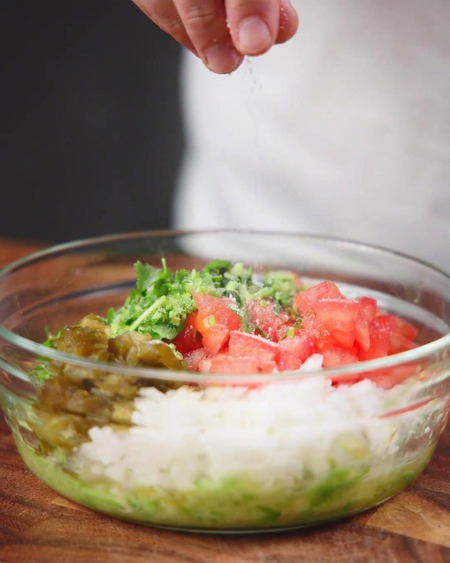 Meersalz wird von oben in eine klare Glasschüssel voller gehackter Tomaten, Zwiebeln, Paprika und Kräuter gestreut.
