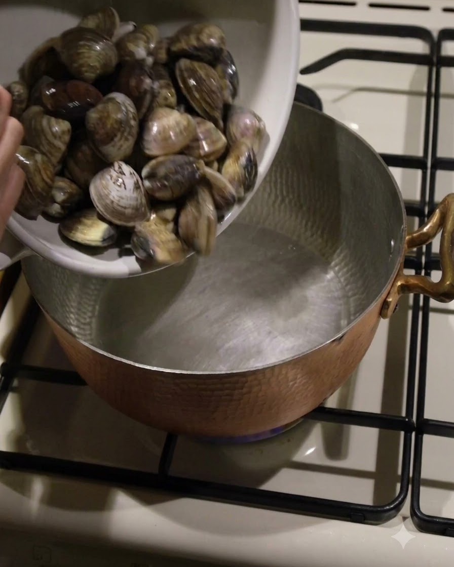 Frische Muscheln werden aus einer weißen Schüssel in einen kupfernen Topf gefüllt.