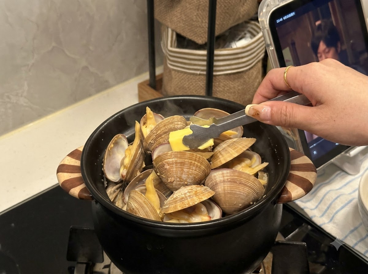Ein kleines Stück Butter wird mit einer Zange in einen mit geöffneten Muscheln gefüllten schwarzen Topf gelegt.
