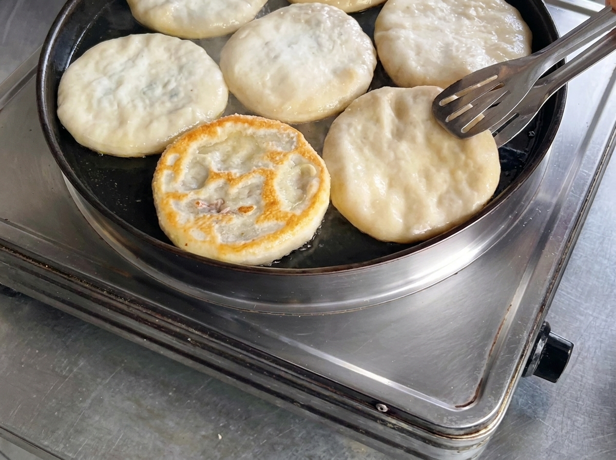 Eine Fleischpastete wird in der Pfanne mit einer Metallzange gewendet.
