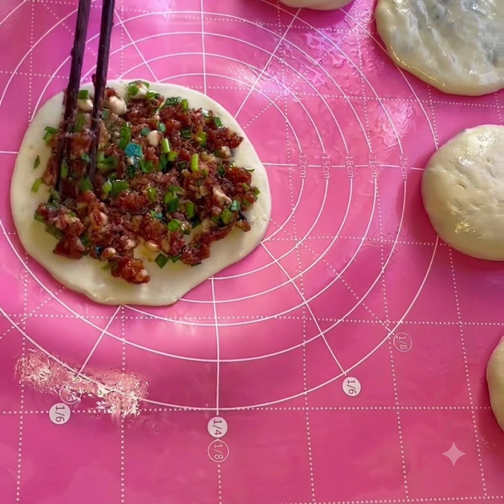 Fleisch- und Schnittlauchfüllung wird mit Essstäbchen gleichmäßig auf einem runden Teigblatt verteilt.
