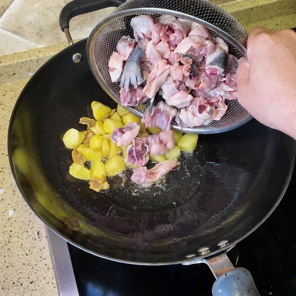 Gehackte rohe Hähnchenstücke werden aus einem Drahtsieb in den Wok mit gebratenen Kartoffeln und Ingwer gegeben.