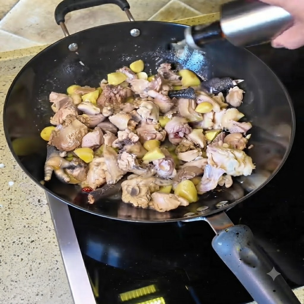 Gelber Wein wird aus einer Flasche in den mit anseuchenden Hähnchenstücken gefüllten Wok gegossen.