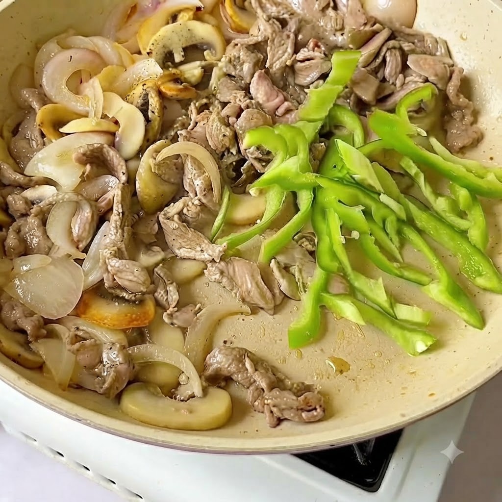 Frische grüne Paprikascheiben werden zusammen mit Rindfleisch und Zwiebeln in die Bratpfanne gegeben.