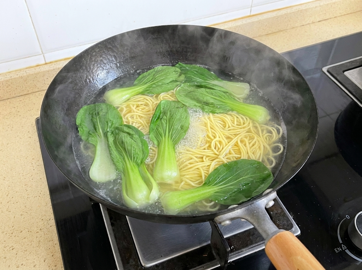 Frische Pak Choi-Blätter schwimmen neben kochenden Nudeln in einem Wok im kochenden Wasser.