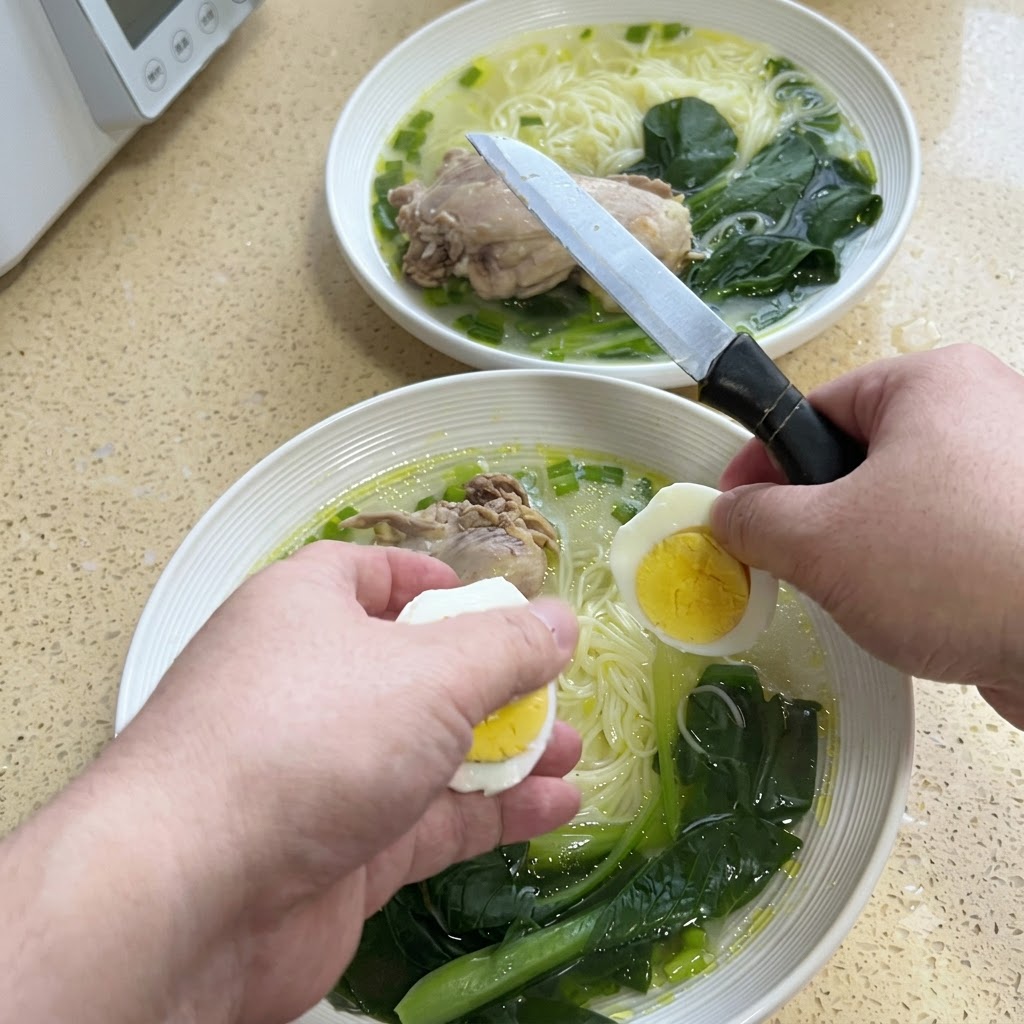 Hände schneiden ein hartgekochtes Ei mit einem Messer über einer Schüssel Nudelsuppe in zwei Hälften.