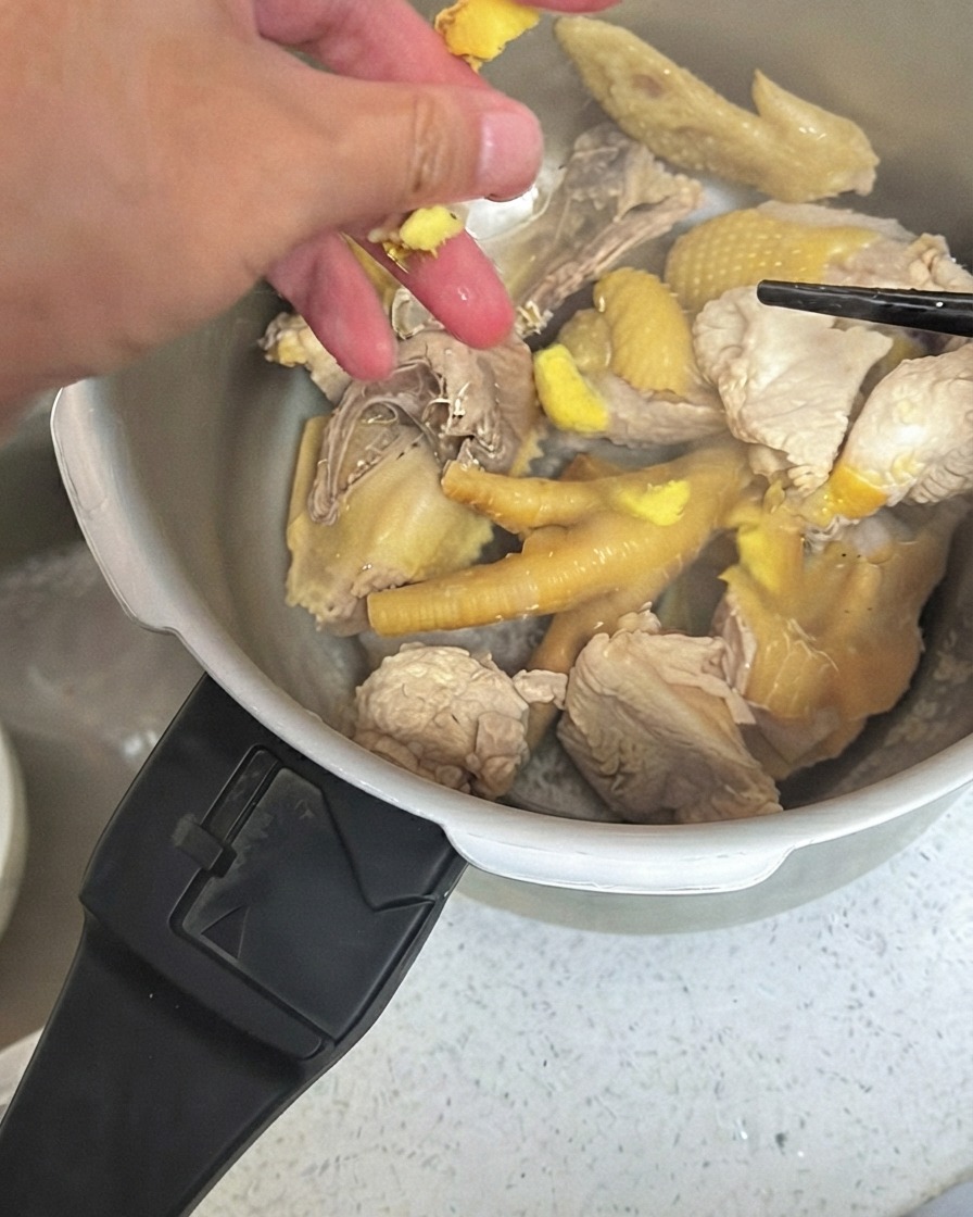 Zerdrückte Ingwerstücke werden über das Hähnchen im Schnellkochtopf verteilt.