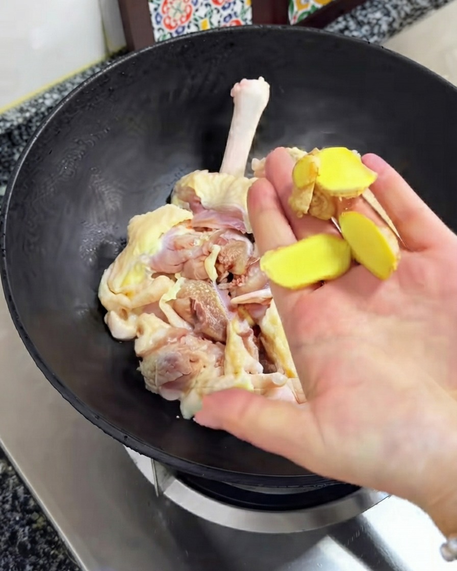 Frische Ingwerscheiben werden über dem rohen Hühnchen im schwarzen Wok gehalten.
