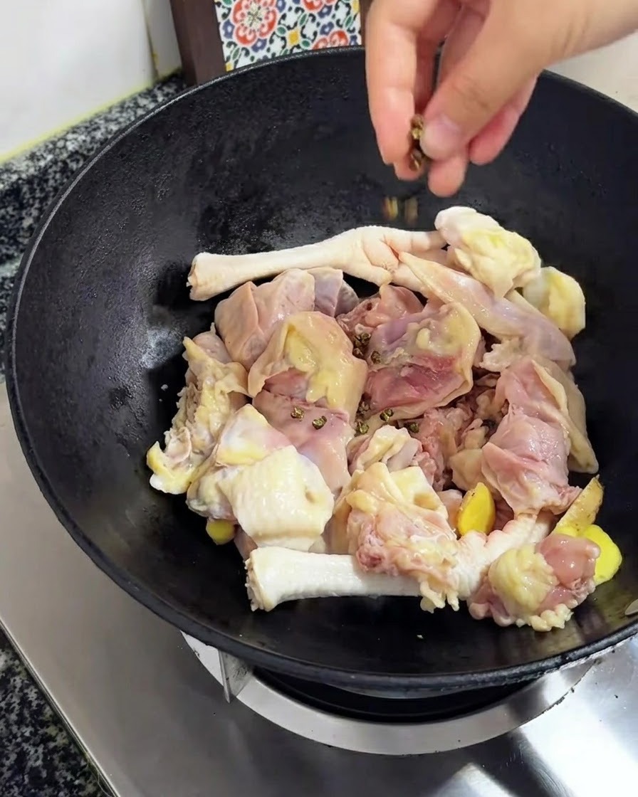 Sichuanpfeffer wird auf das Hühnchen und den Ingwer im Wok gestreut.