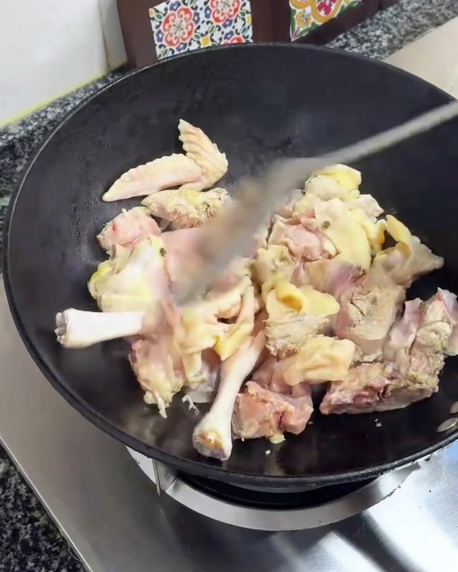 Hühnerstücke werden mit einem Pfannenwender in einem schwarzen Wok auf dem Herd angebraten.