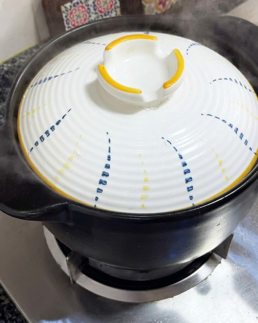 Ein weißer Deckel mit blau-gelben Mustern wird fest auf einen schwarzen Tontopf gesetzt.