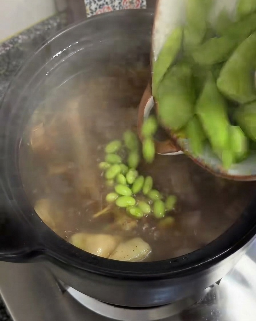 Dicke Scheiben grünen Celtuce werden aus einer Schüssel in einen köchelnden Suppentopf geschüttet.