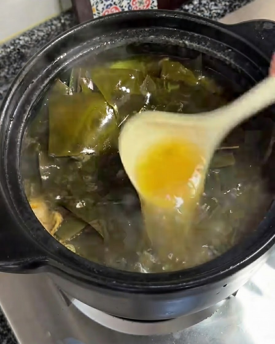 Eine Schöpfkelle entfernt eine Schicht gelbliche Öls von der brodelnden Oberfläche der Suppe.