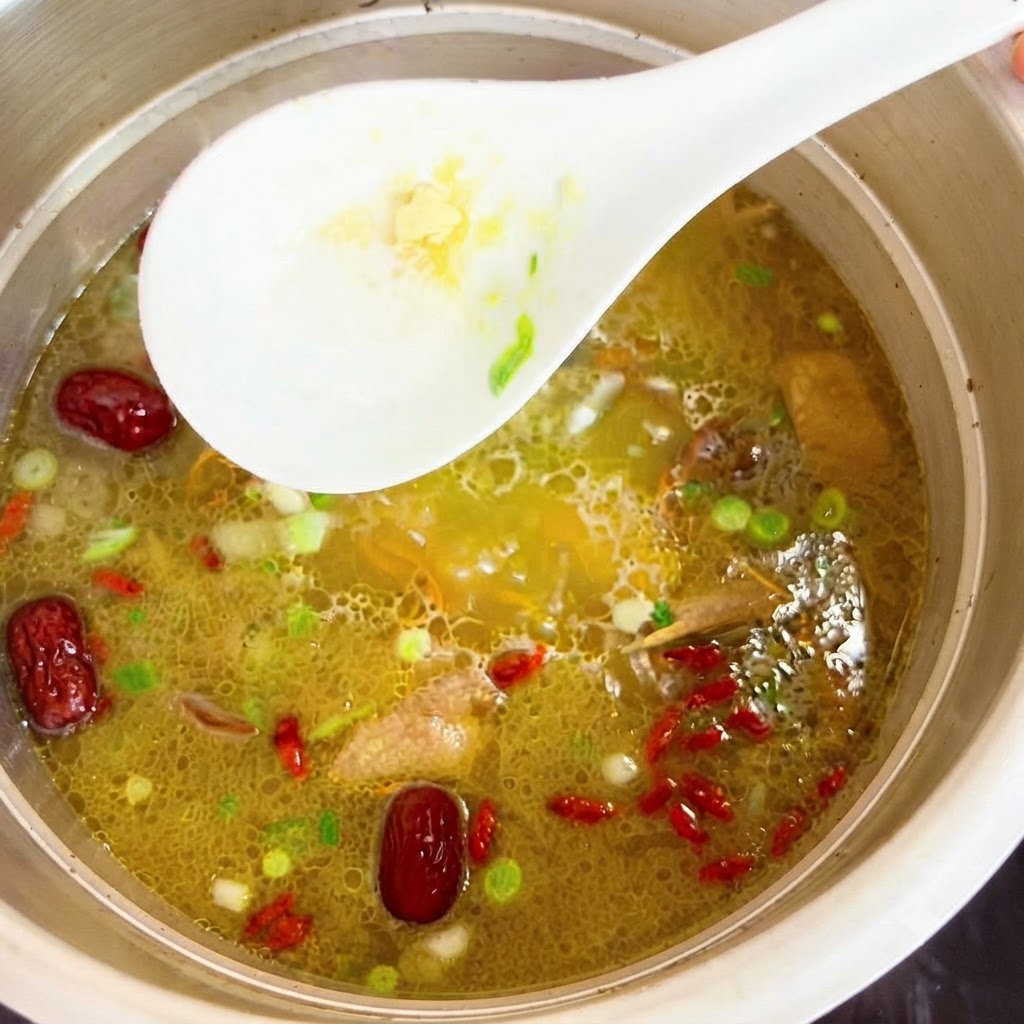 Hühner-Essenz wird mit einem weißen Löffel in den Topf mit heißer Hühnersuppe eingerührt.