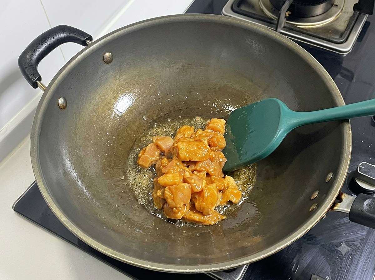 Gewürfelte marinierte Hähnchenbrust wird in einem heißen Wok mit einem grünen Pfannenwender angebraten.
