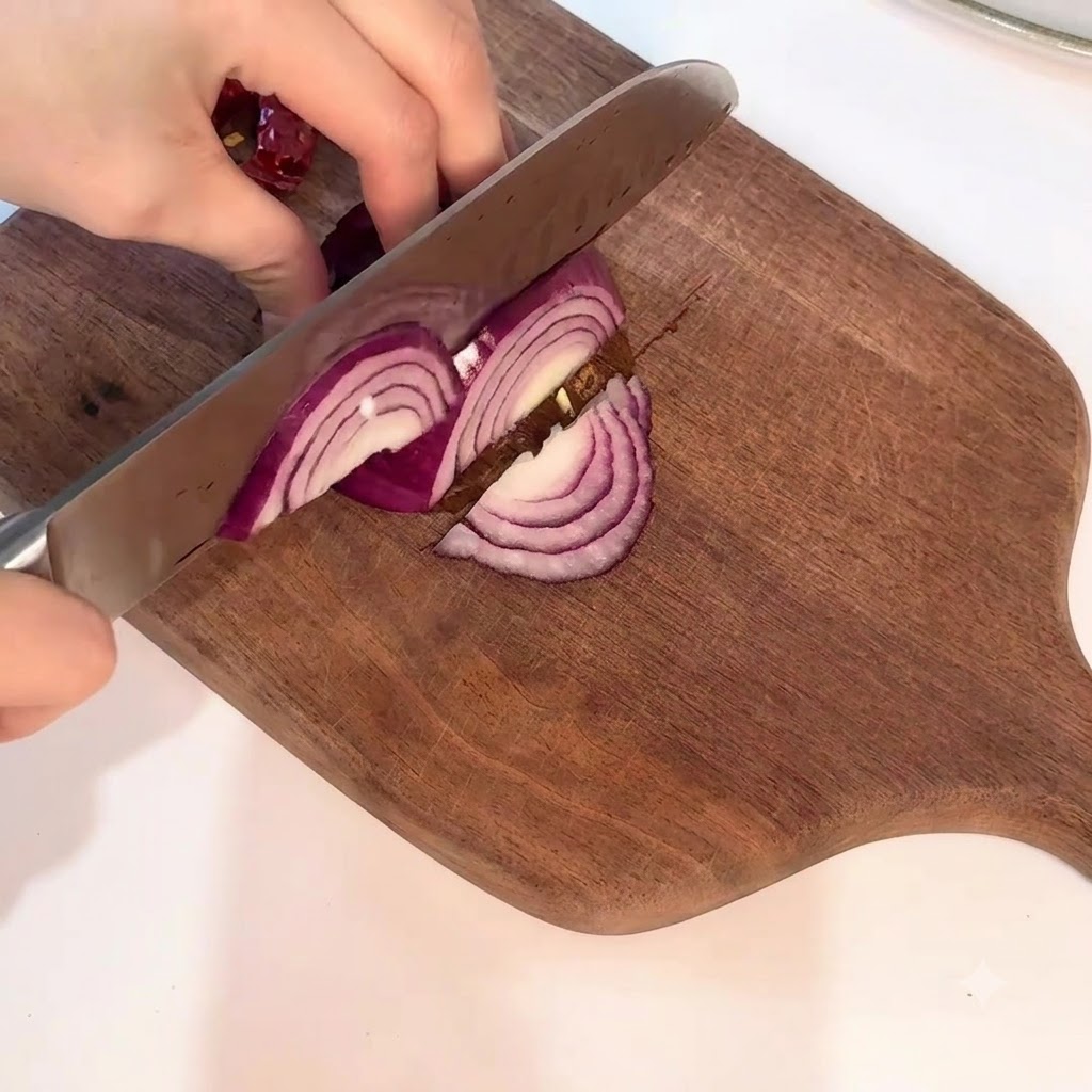 Eine rote Zwiebel wird mit einem Messer sorgfältig in saubere Halbmonde auf einem Holzbrett geschnitten.