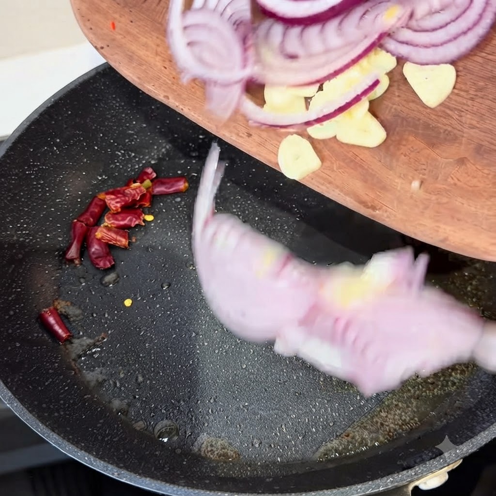 Rote Zwiebelscheiben, Knoblauchzehen und getrocknete Chilischoten werden von einem Holzbrett in eine heiße Bratpfanne gegeben.