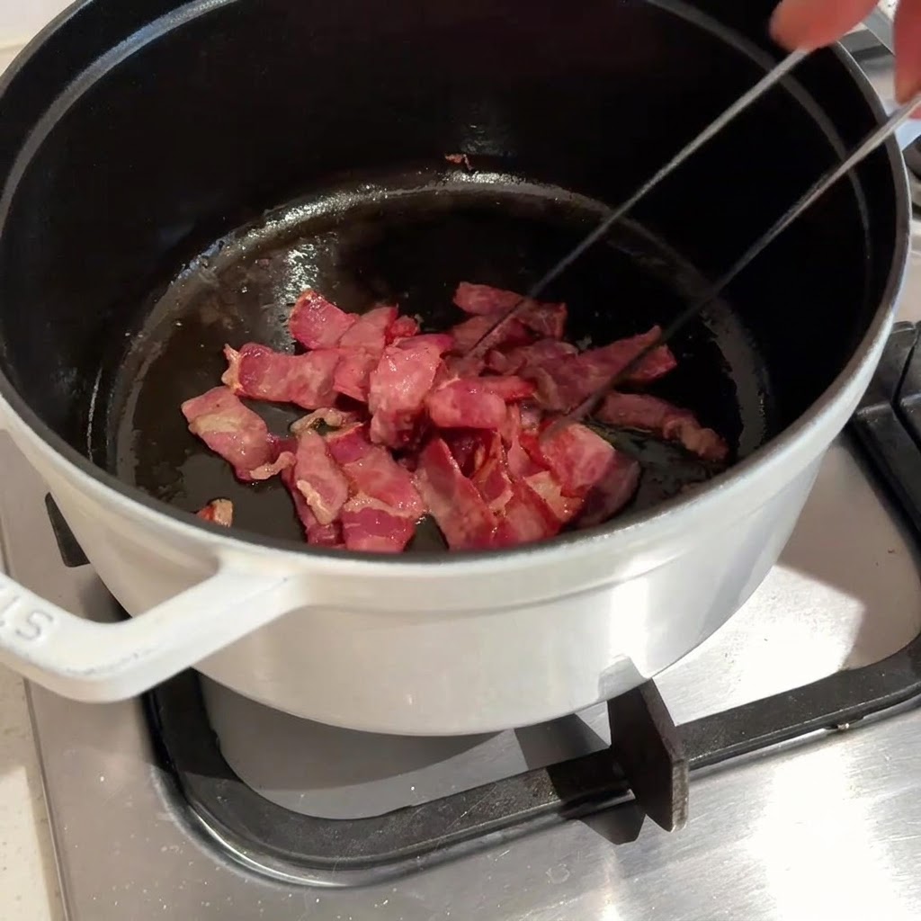 Gehackter Bacon wird in einem dunklen Topf mit einer Zange angebraten.