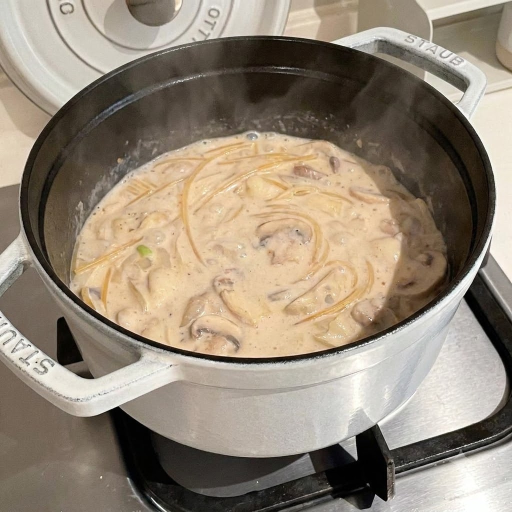 Spaghetti kochen in einer köchelnden, cremigen Brühe in einem weißen Topf.