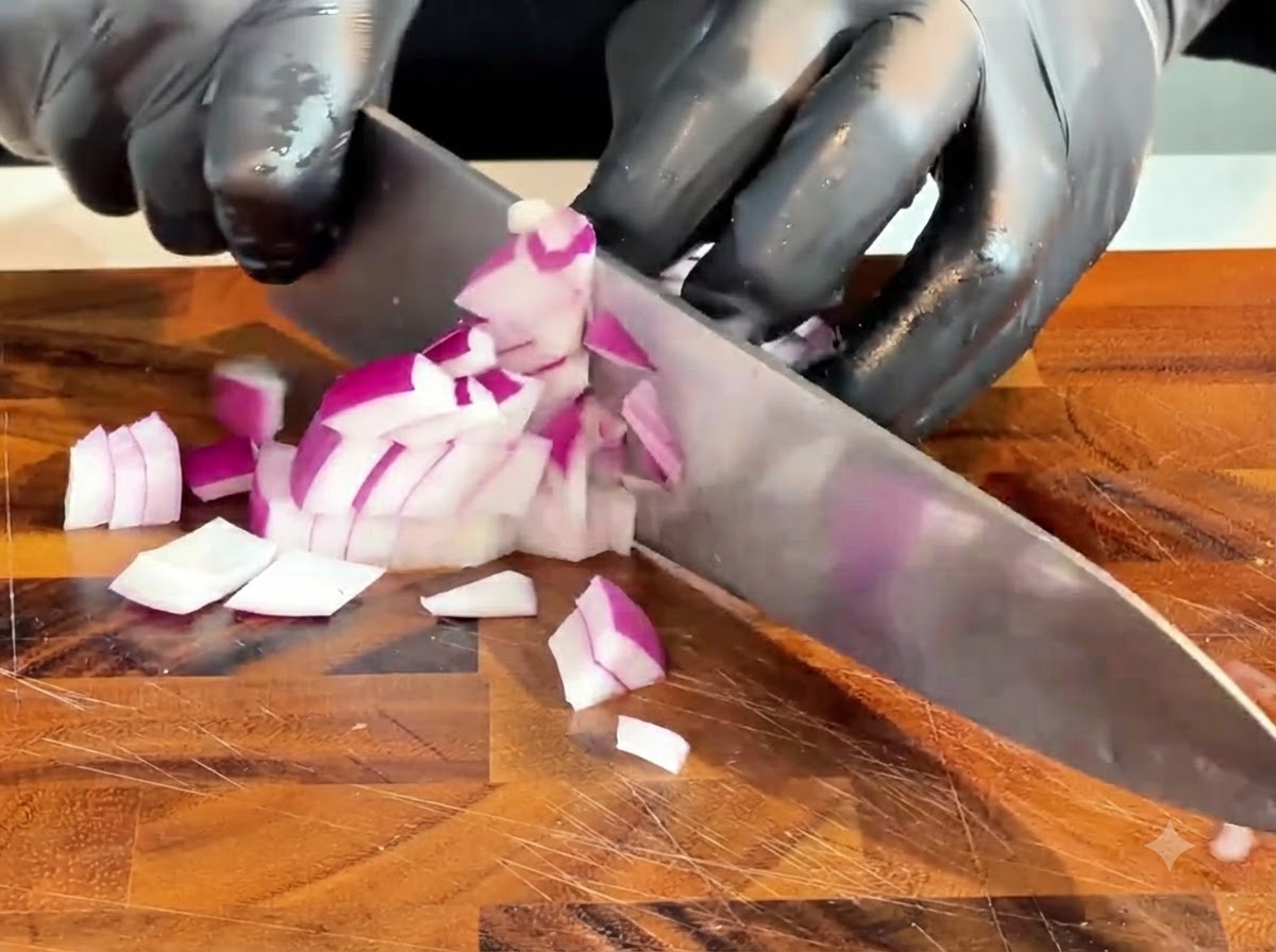 Ein Messer schneidet eine rohe rote Zwiebel in kleine Stücke auf einem Holzschneidebrett.