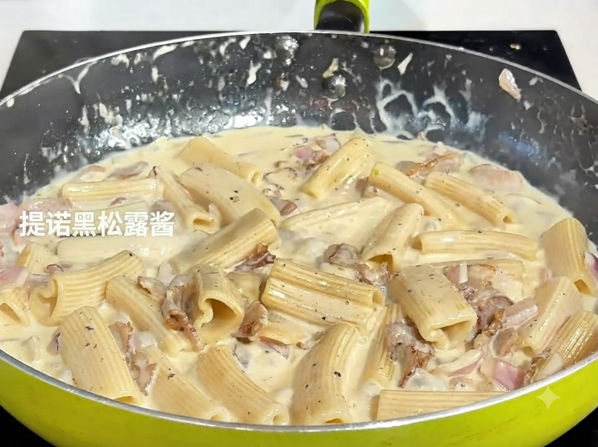 Ein Löffel dunkle schwarze Trüffelpaste wird zu der köchelnden Pastamischung in eine Pfanne gegeben.