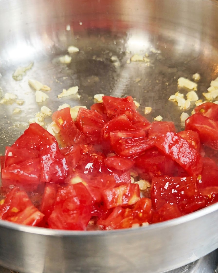 Frische gewürfelte rote Tomaten werden mit Knoblauch in einer Metallpfanne angebraten.