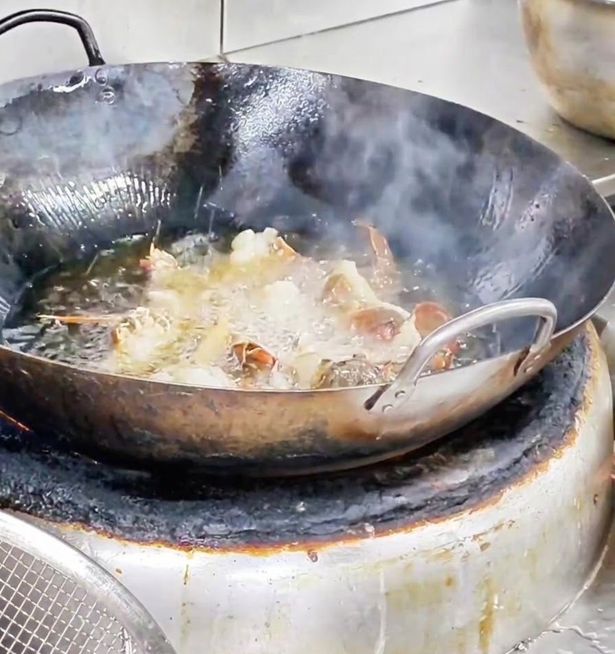 Hummerstücke frittieren lebhaft in einem Wok gefüllt mit blubberndem, heißem Öl.