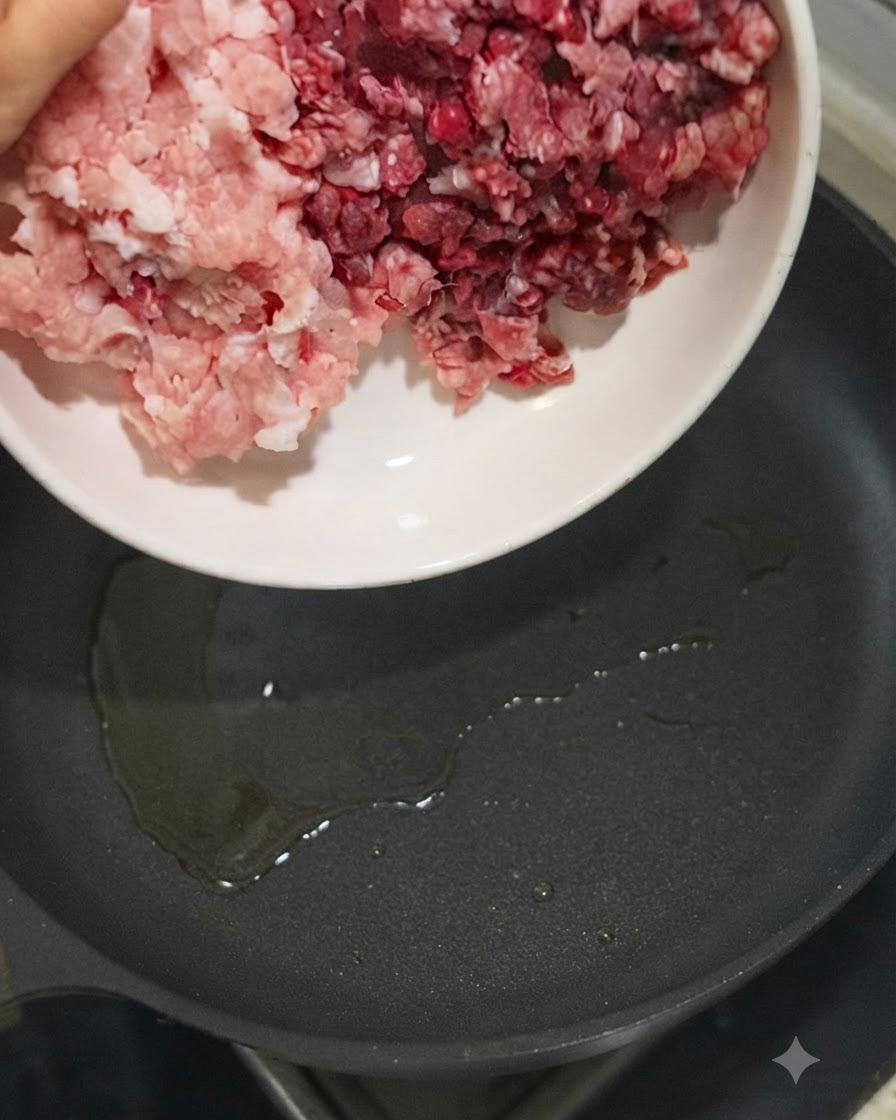 Schweine- und Rinderhackfleisch wird aus einer weißen Schüssel in eine heiße Pfanne mit Öl gegeben.