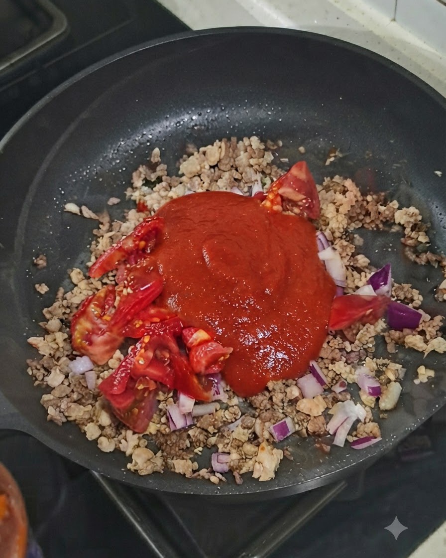 Ein Klecks Tomatenmark liegt auf der Fleisch-Gemüse-Mischung in der Pfanne.