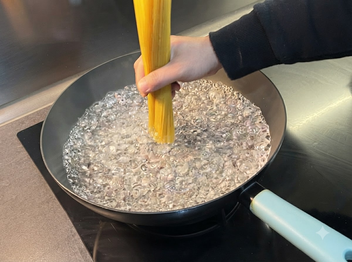 Eine Hand hält ein Bündel trockene Spaghetti senkrecht in einen breiten Topf mit kochendem Wasser.