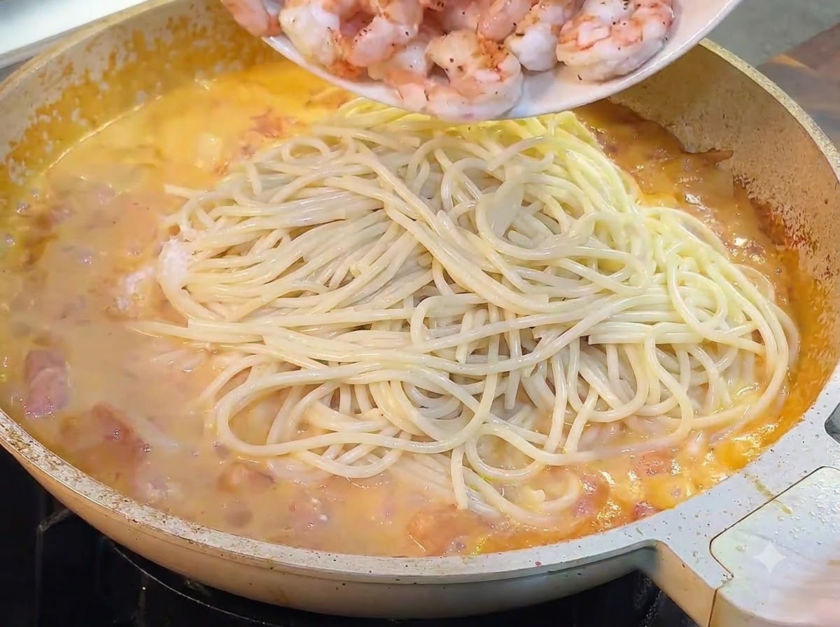 Gekochte Garnelen werden von einem Teller in die Pfanne mit Spaghetti und Sauce geschüttet.