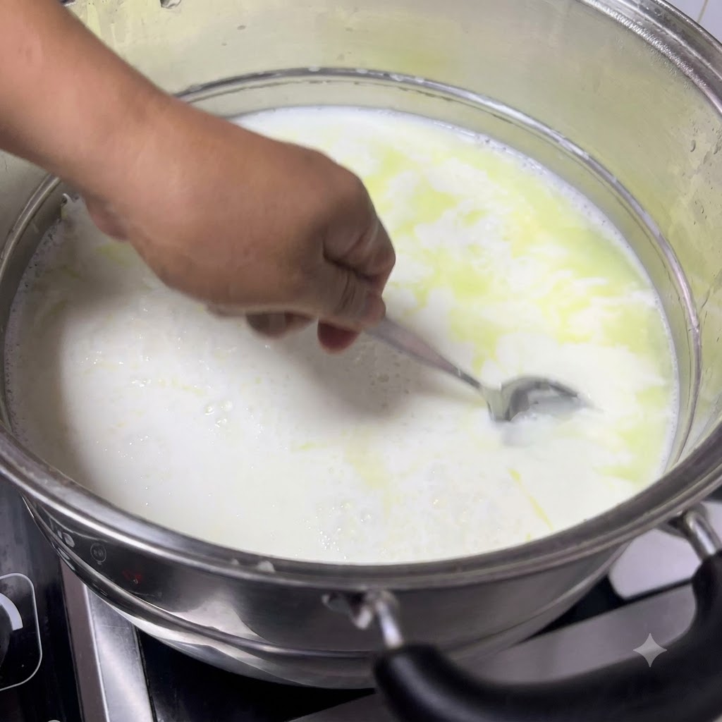 Ein Löffel schöpft geronnene Milch aus dem Topf, wobei weiche weiße Körnchen zu sehen sind, die sich von der gelblichen Molke trennen.