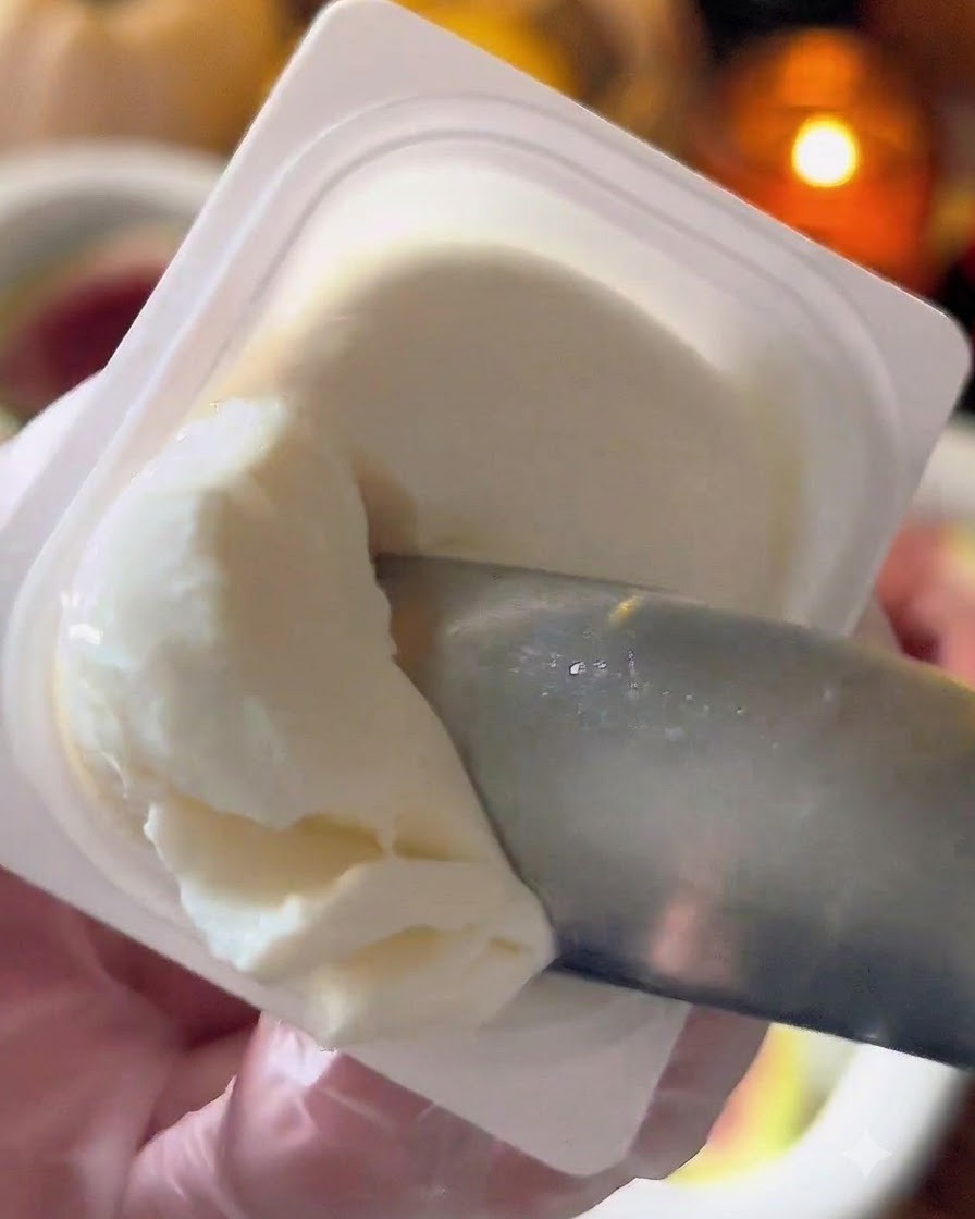 Ein kleiner Löffel entnimmt weißen Labneh-Käse aus einem Behälter.