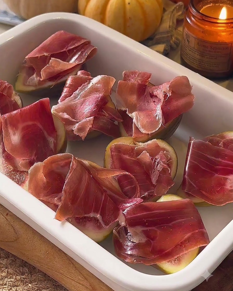 Vorbereitete Feigen mit Prosciutto in einer weißen Auflaufform angeordnet.